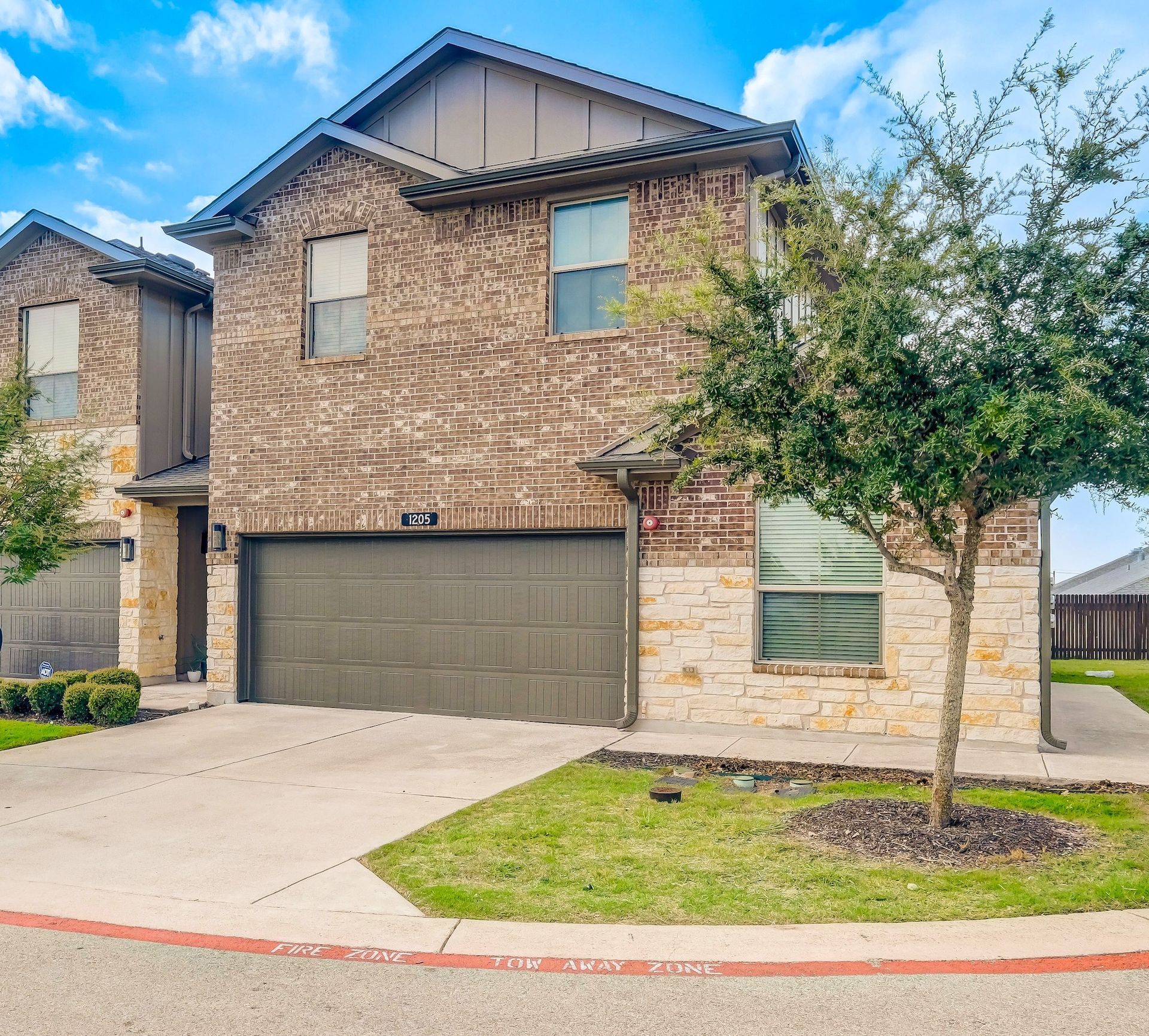 Two-story brick house with attached garage, beige stone accents, and small front yard with a tree.