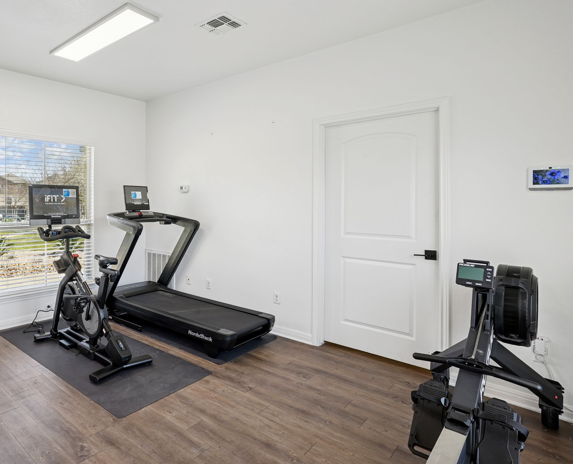 Home gym with exercise equipment: stationary bike, treadmill, rower, and computer.