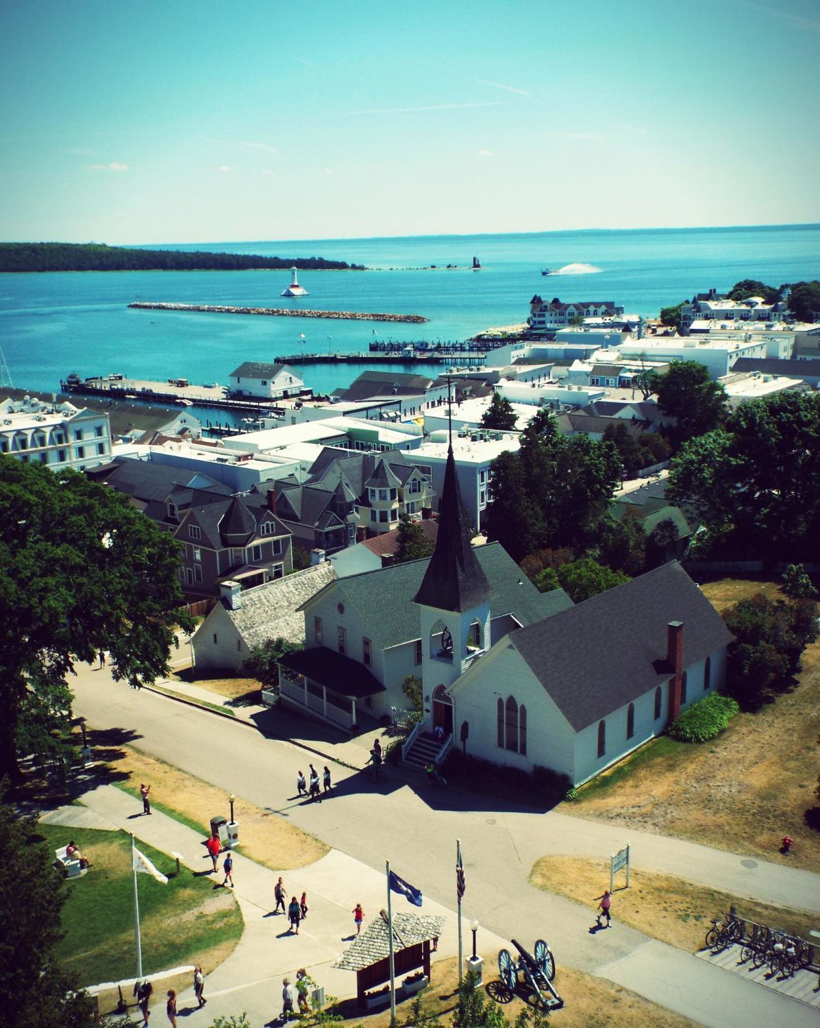 Overhead view of a white church with steeple overlooking a town and turquoise water. Clear, sunny day.