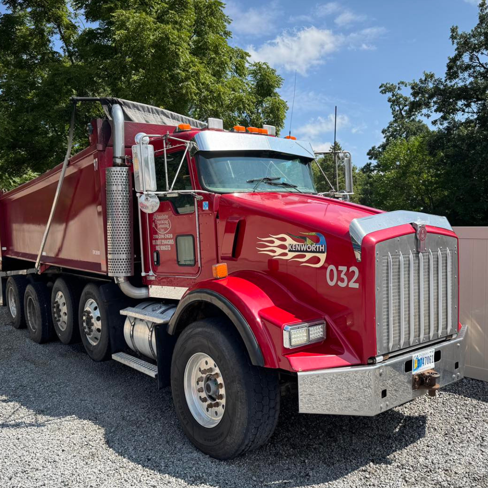 Red dump truck parked outside, under a blue sky.