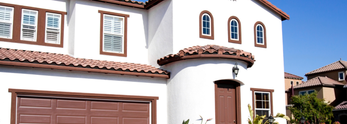 White stucco house with brown trim, arched windows, and red tile roof on a sunny day.