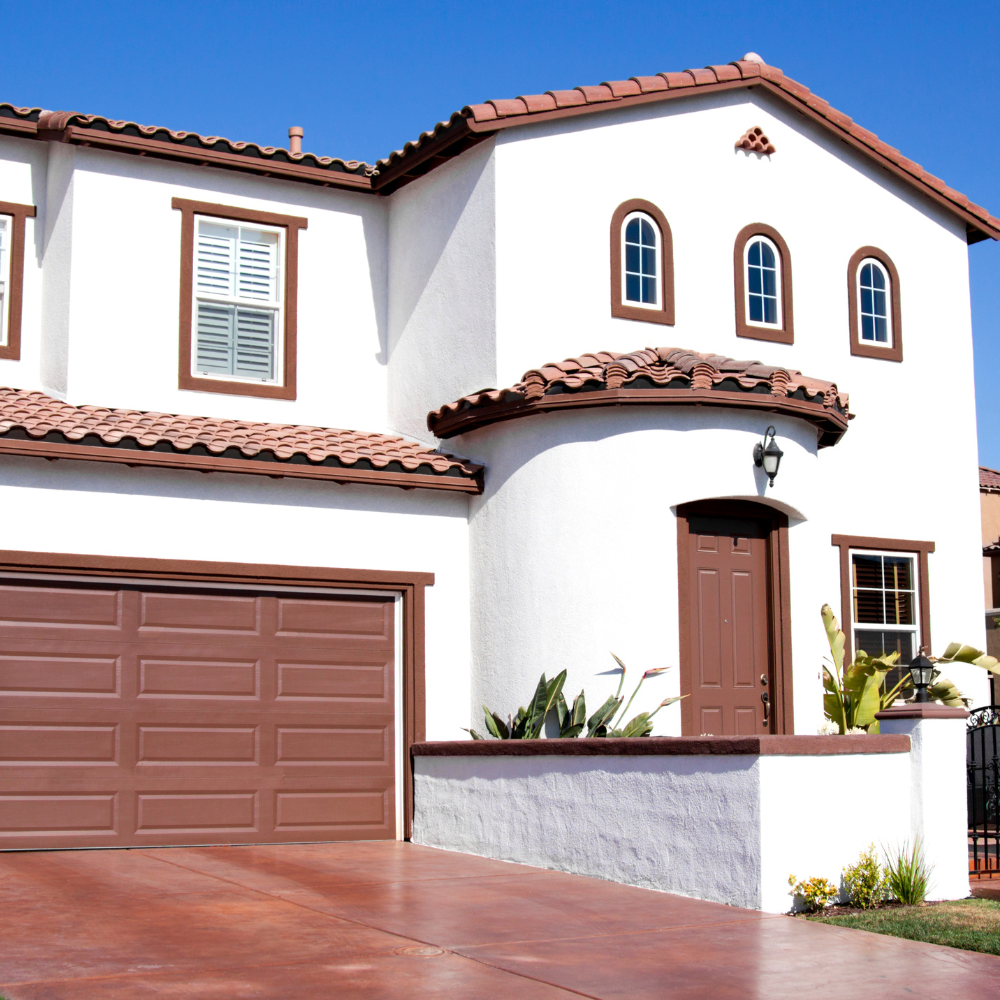 Two-story white house with brown trim and a red tile roof. Brown garage door and front door.