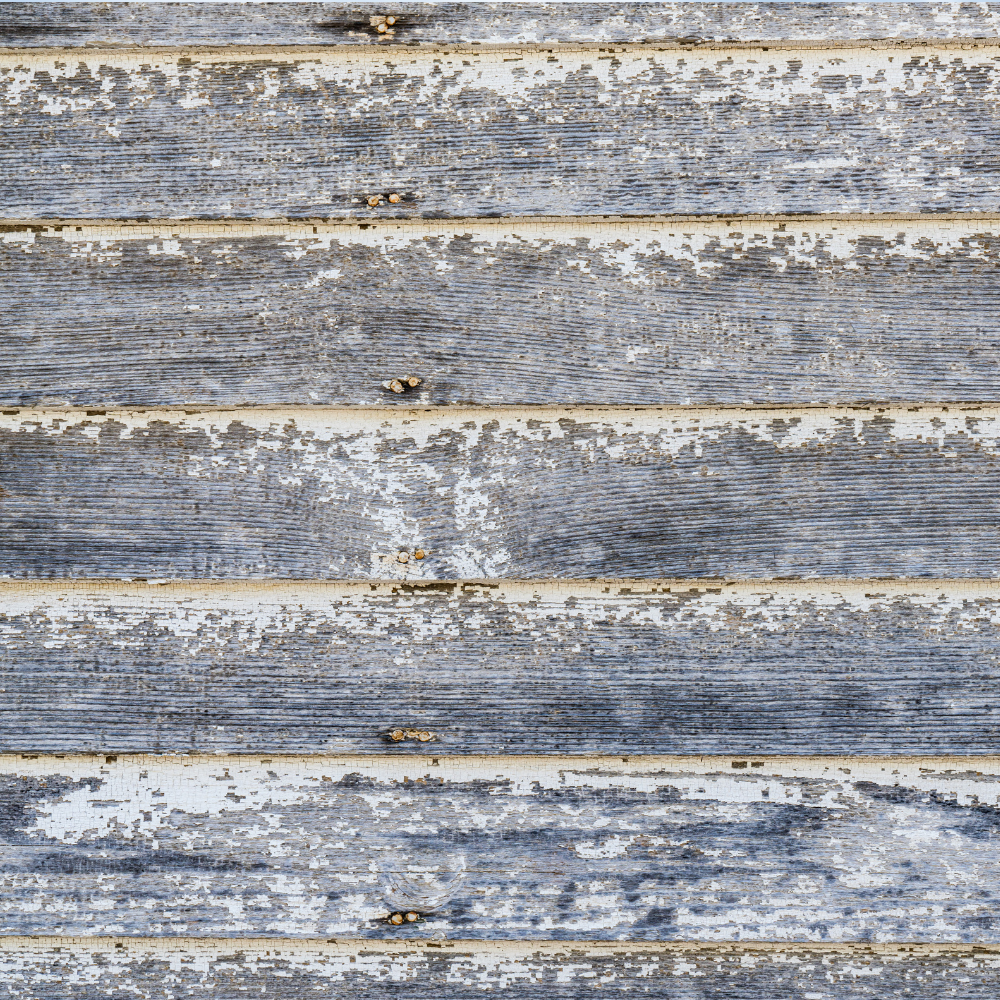 Weathered, gray wooden planks with peeling white paint, creating a textured, rustic wall.