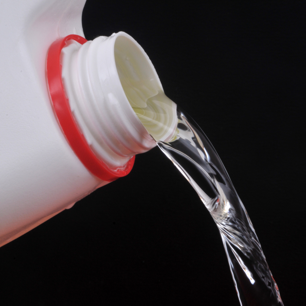 Clear liquid pouring from a white container with a red ring, against a black background.