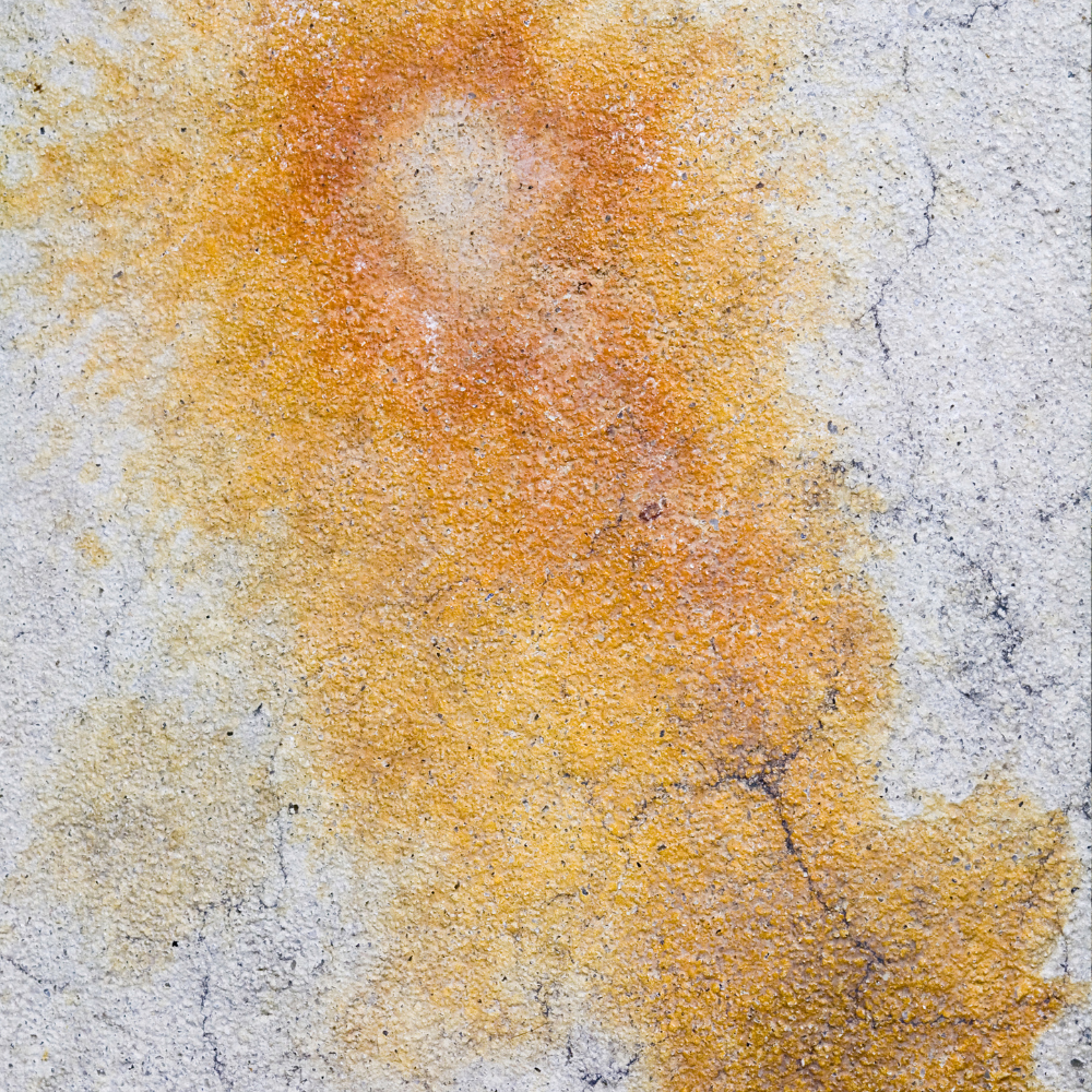 Yellow-orange stain on a cracked, gray concrete surface.