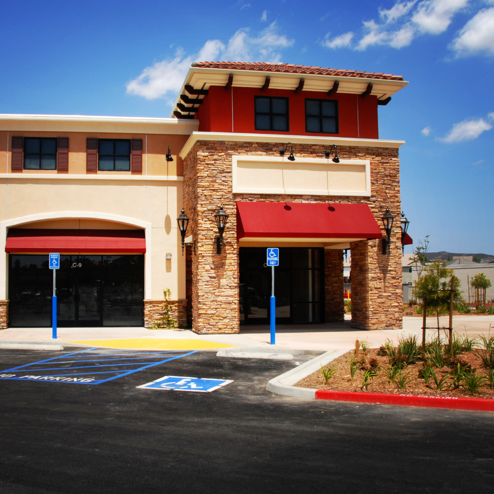 Exterior view of a building with tan stucco, red awnings, and accessible parking.