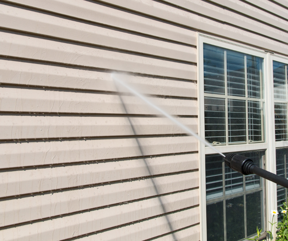 Power washer spraying siding on a house next to a window.