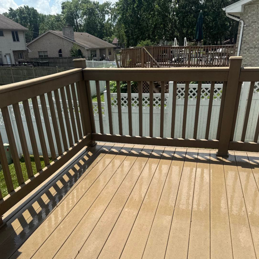 Brown deck with brown railing, white fence, and green grass in a suburban backyard.