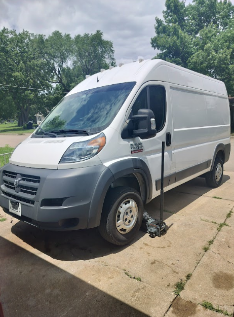 White Ram ProMaster van with a jack under the front wheel, parked on a concrete surface.