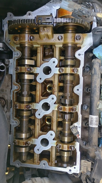 Overhead view of engine's cylinder head, showcasing camshafts, timing chain, and oil-stained components.