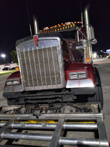 Red and chrome Kenworth semi-truck parked at night, with large grill and exhaust stacks.