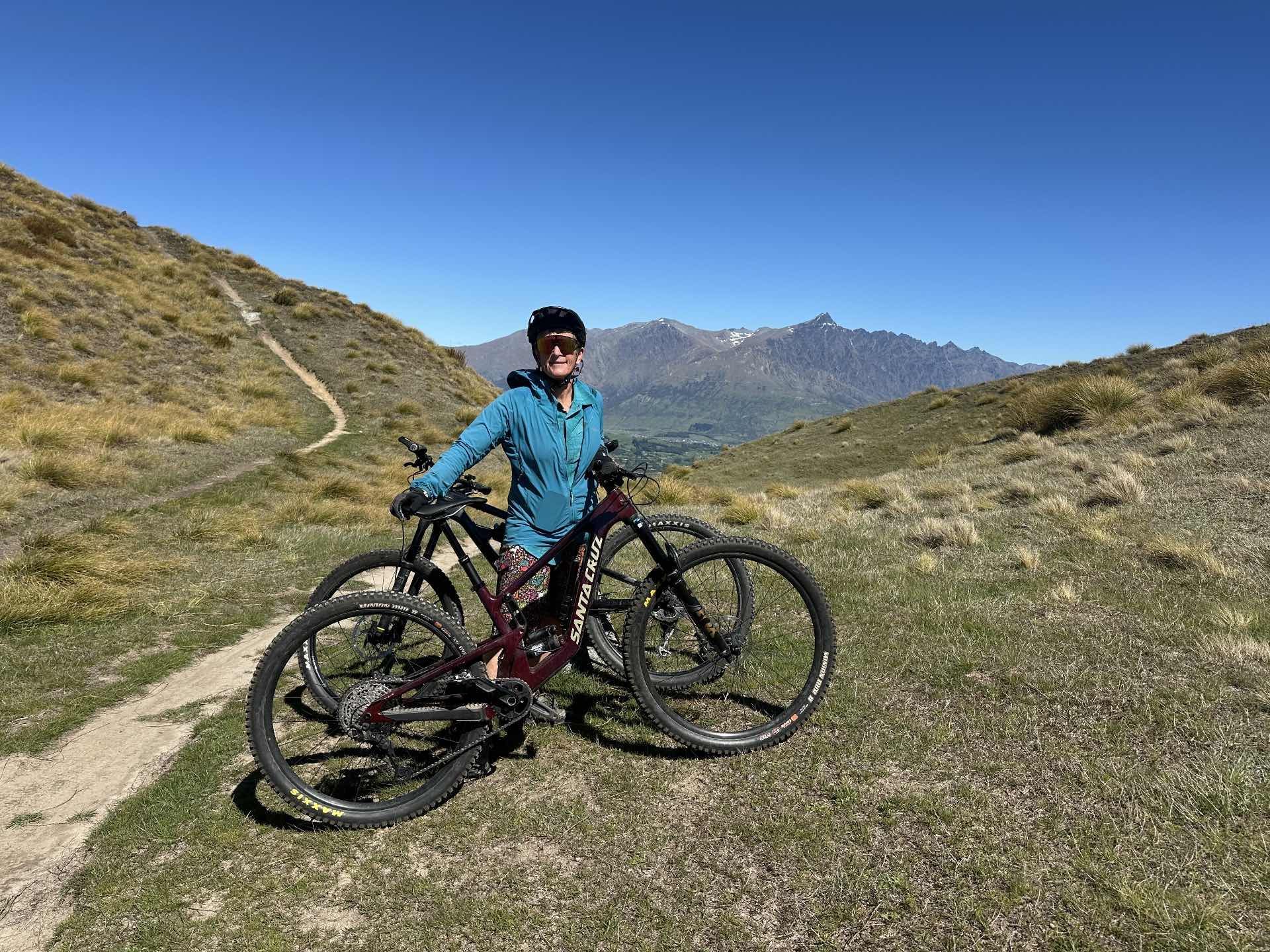 Person with mountain bikes on a trail, mountains in background.
