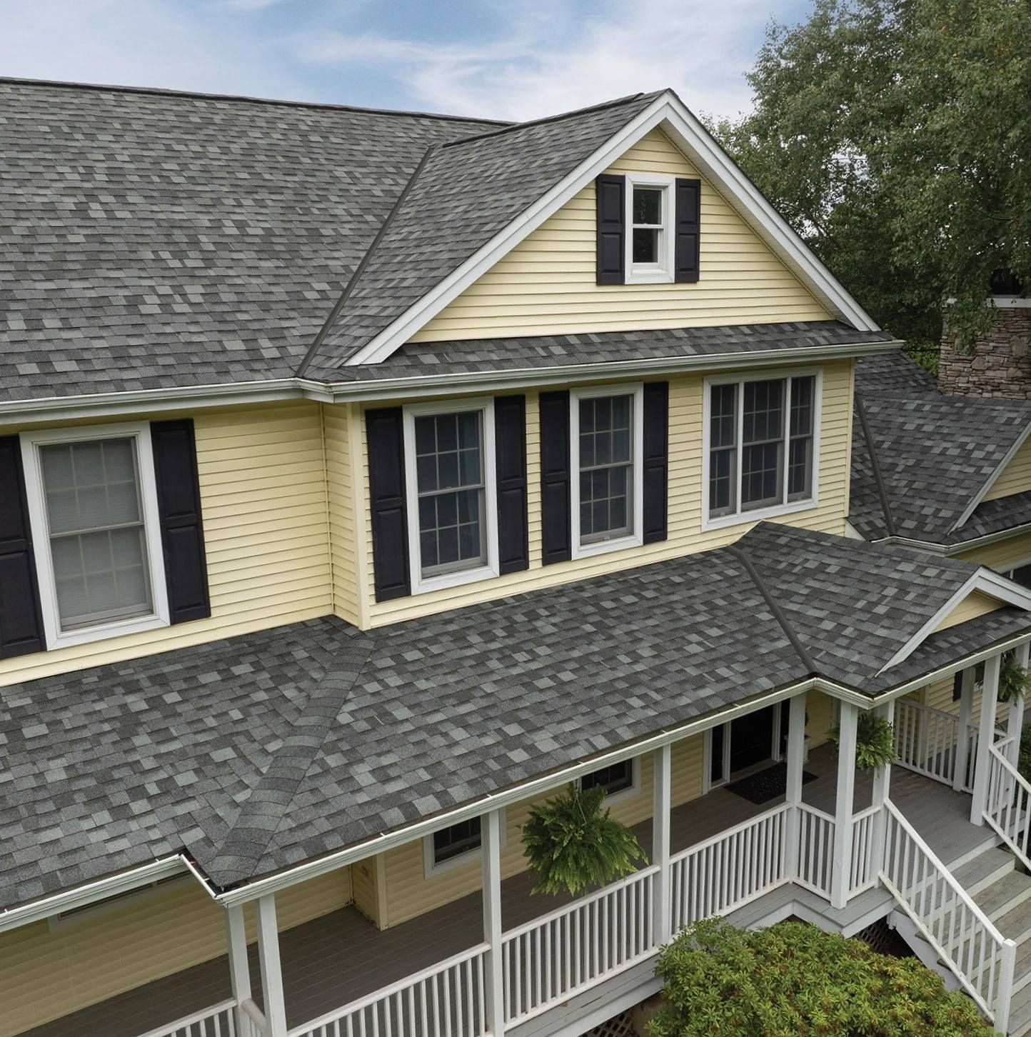 Yellow house with gray roof, black shutters, and a porch.