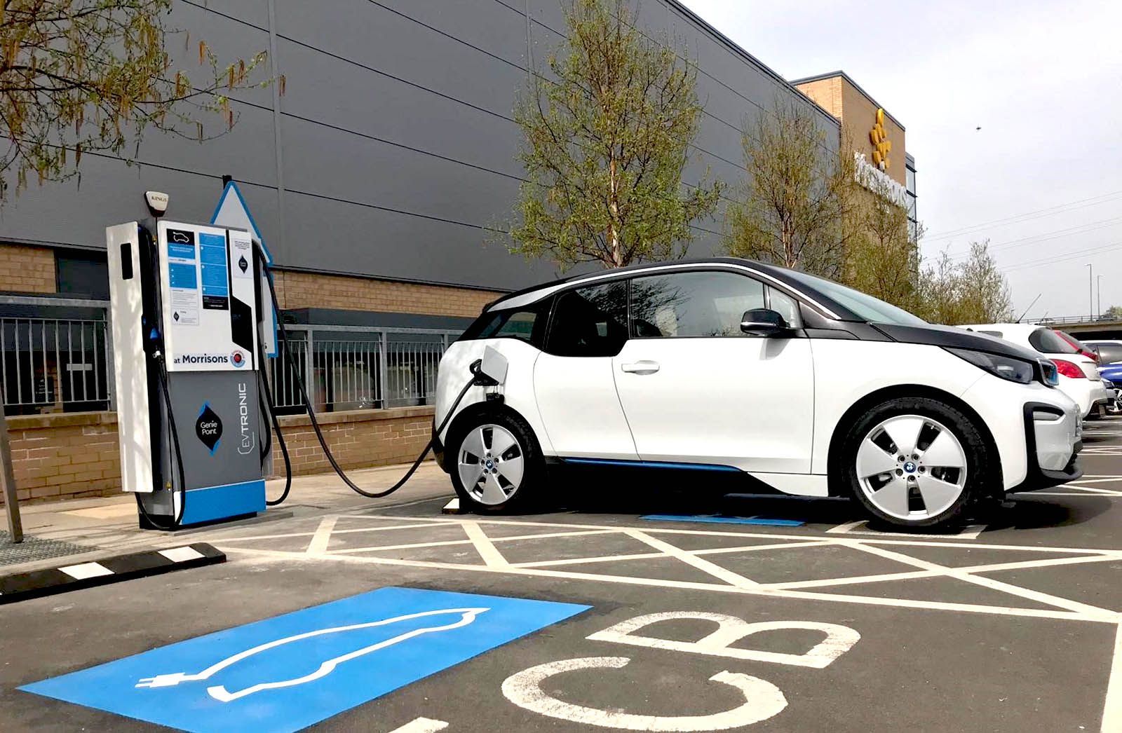 A white electric vehicle is being charged at a charging station in a Morrisons car park