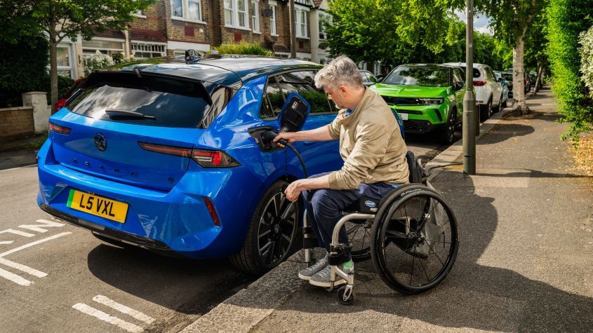 Blue Ev car with a man in a wheel chair besdie it