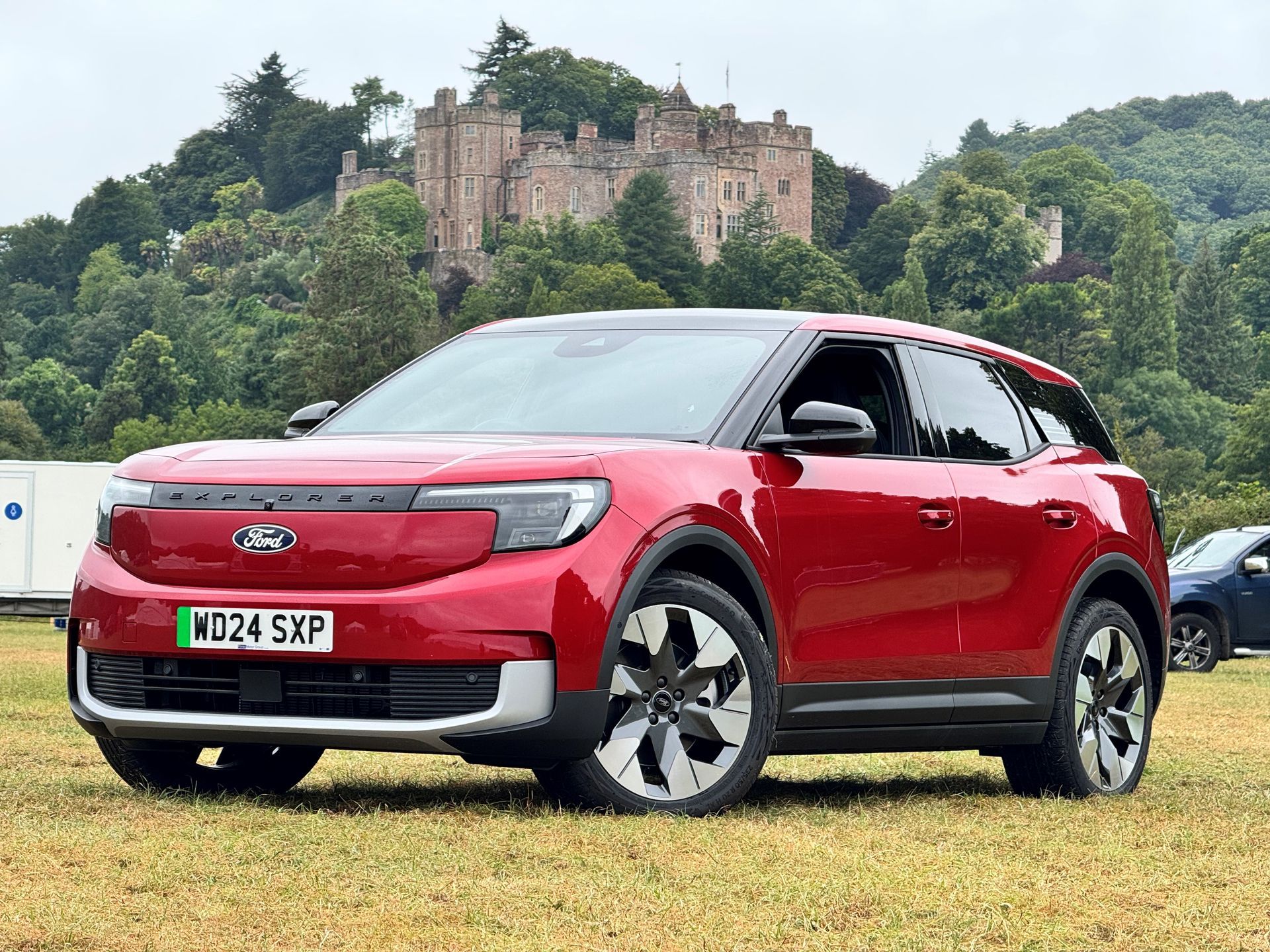 A red ford explorer is parked in a field in front of a castle.