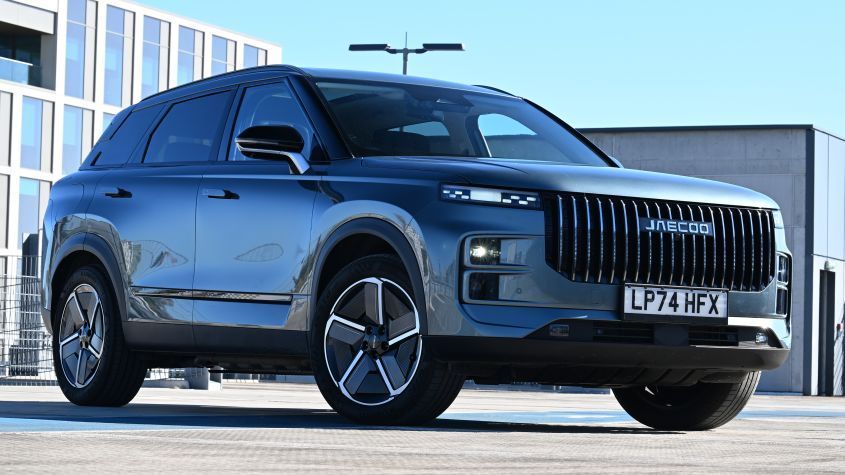 photo of a jaecoo with an glass office building behind it 