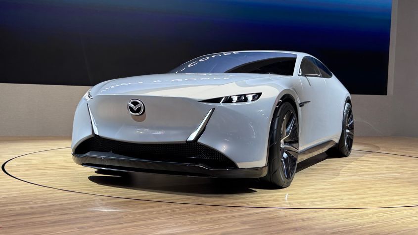 Light blue Mazda electric concept car on a rotating platform, front view.