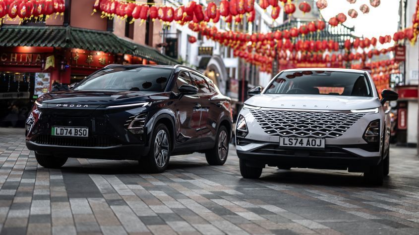 A black and white OMODA next to each other in a street with chinese lanterns above them.