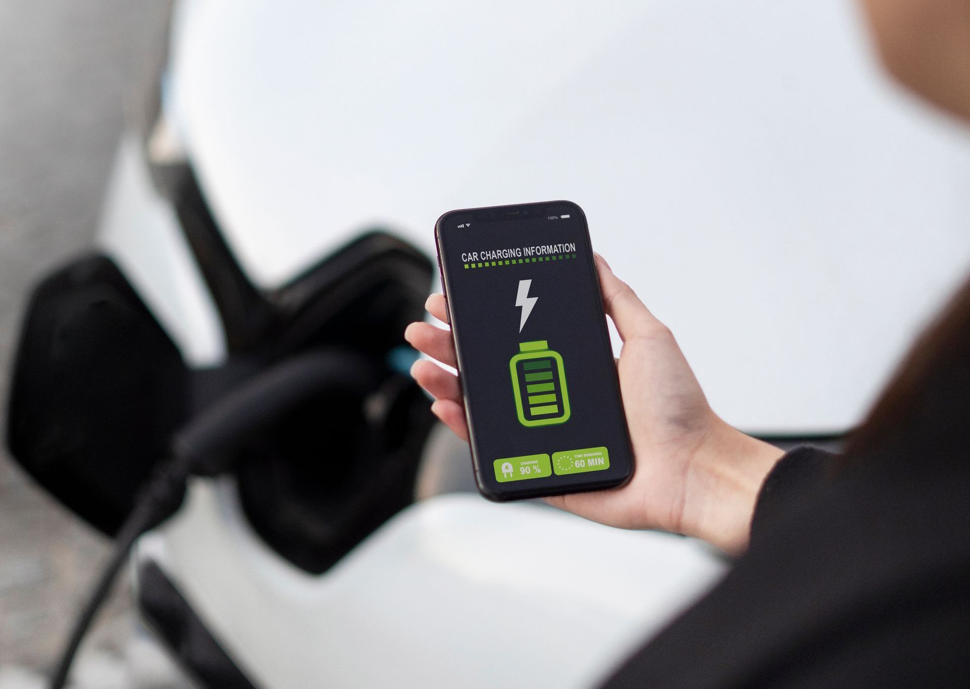 A person holding a phone in front of a electric car.