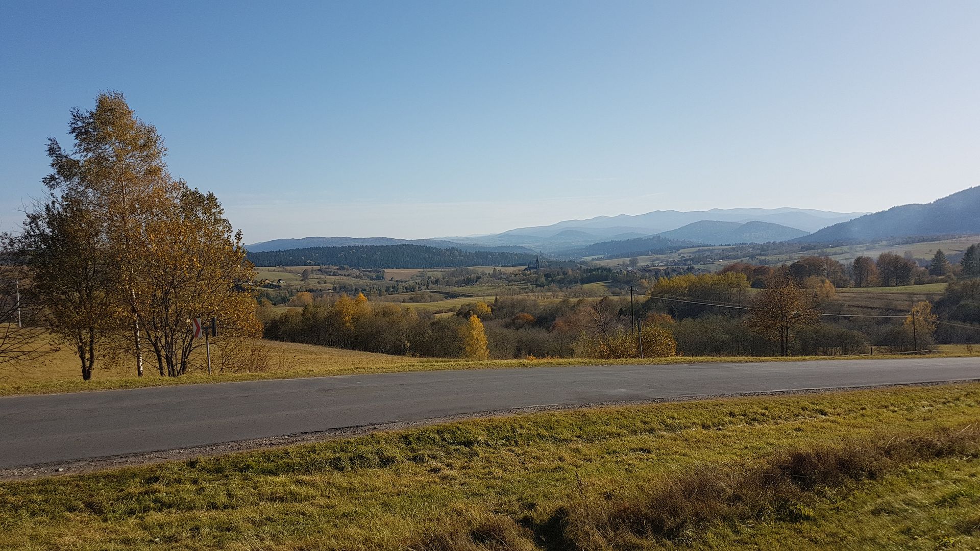 A road going through a grassy field with mountains in the background.