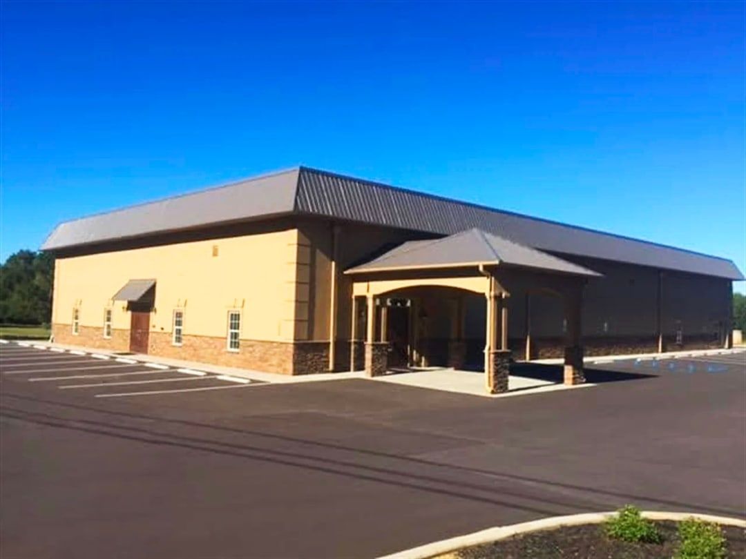Tan building with brown metal roof and a covered entrance under a blue sky.