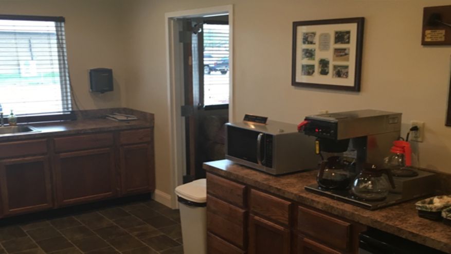 A small break room with a sink, cabinets, microwave, and coffee maker. A door leads outside.