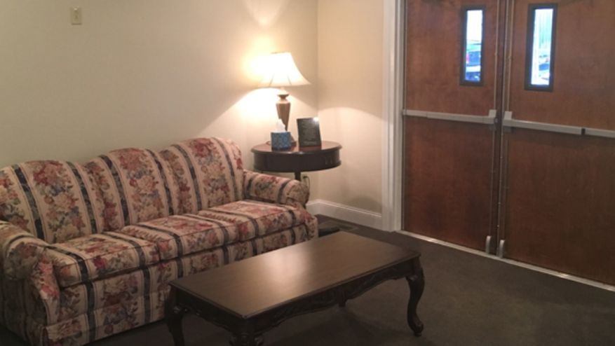 Cozy seating area with floral sofa, lamp on small table, and dark wood doors.