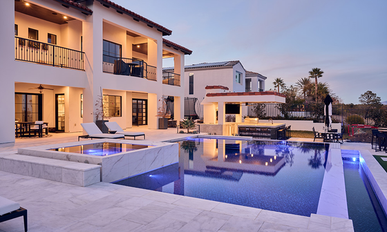 Luxury white villa beside a lit blue pool at dusk