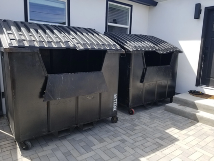 Two large black dumpsters with corrugated lids on a patio.