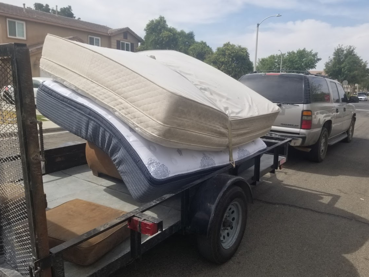 A trailer loaded with two mattresses and a vehicle parked on a street.