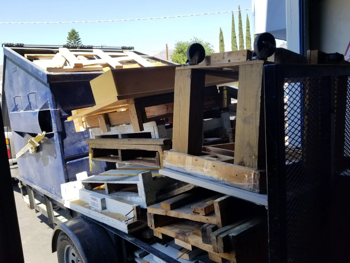 Blue dumpster overflowing with wooden pallets and debris, likely construction waste.