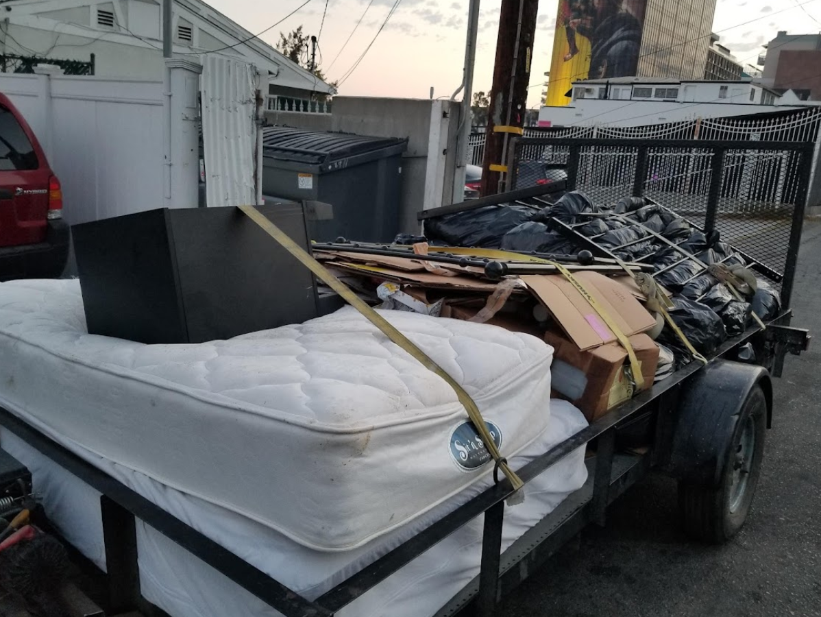 A trailer loaded with a mattress, black box, cardboard, and trash bags.