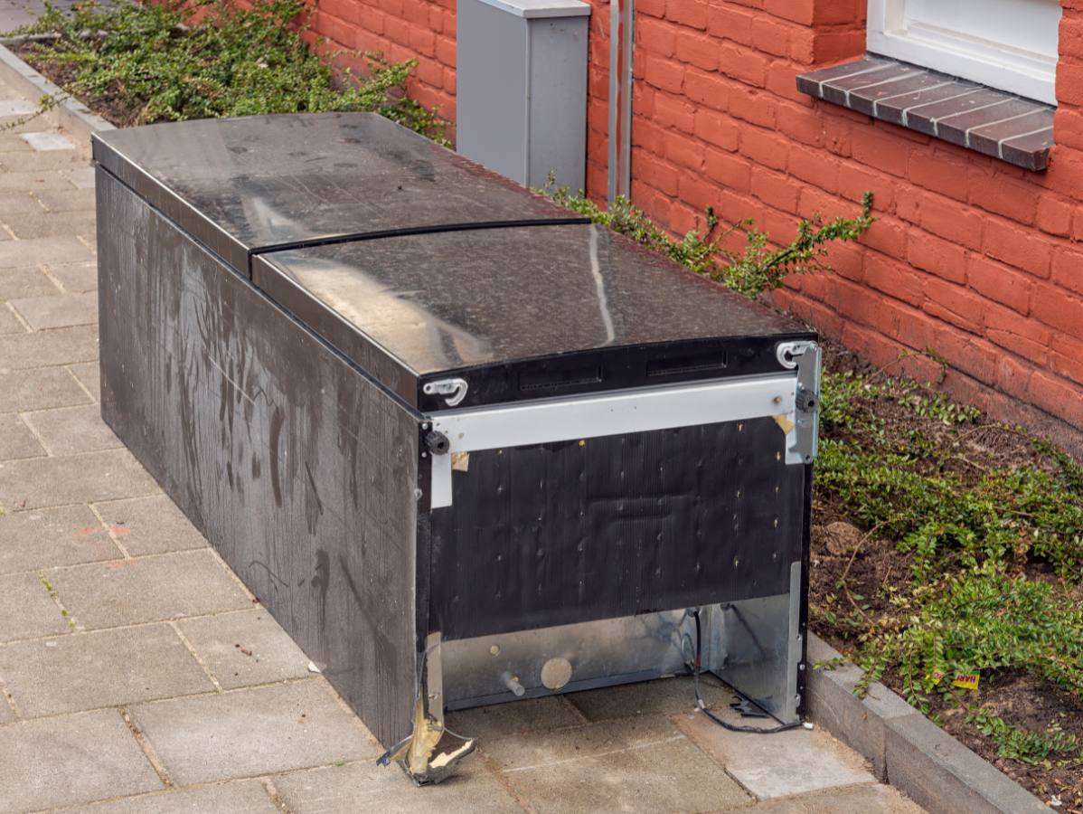 Black recycling container with hinged lids on a brick patio.