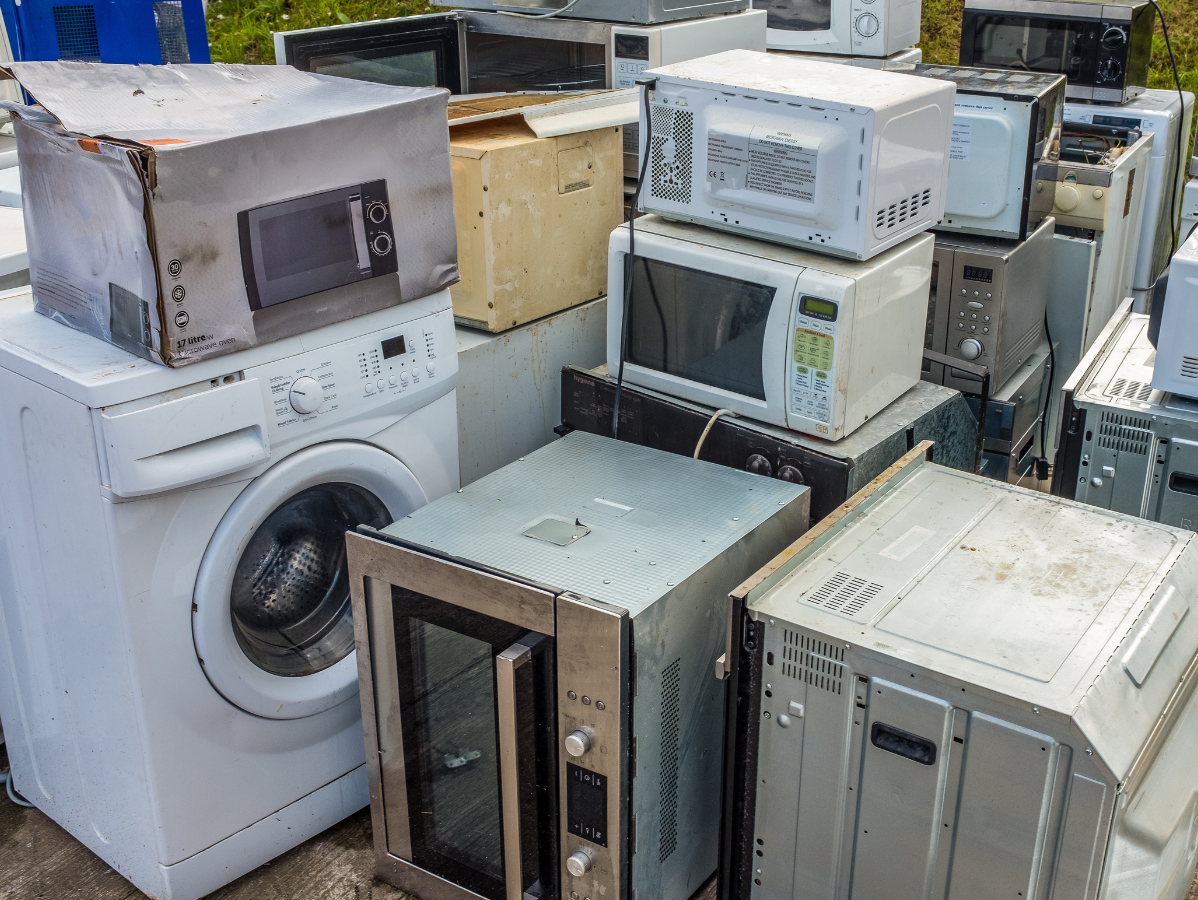 Pile of discarded appliances including microwaves and a washing machine.