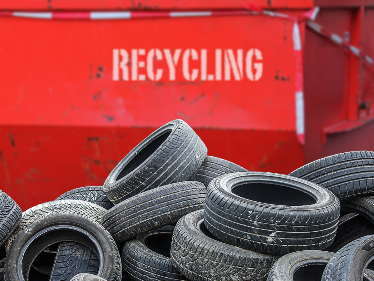 Pile of used tires in front of a red recycling container labeled