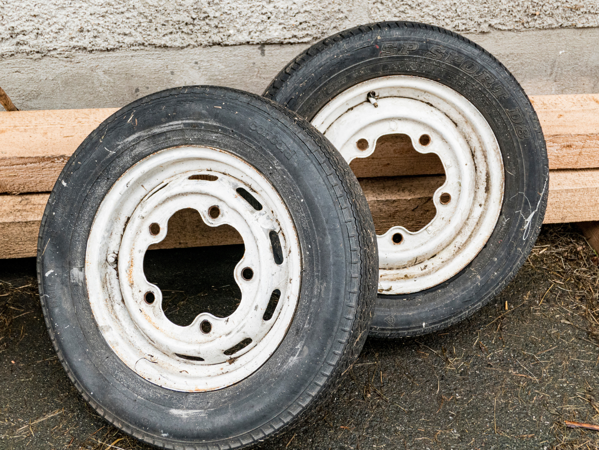 Two white-rimmed, black-tired wheels against a weathered wood and concrete background.