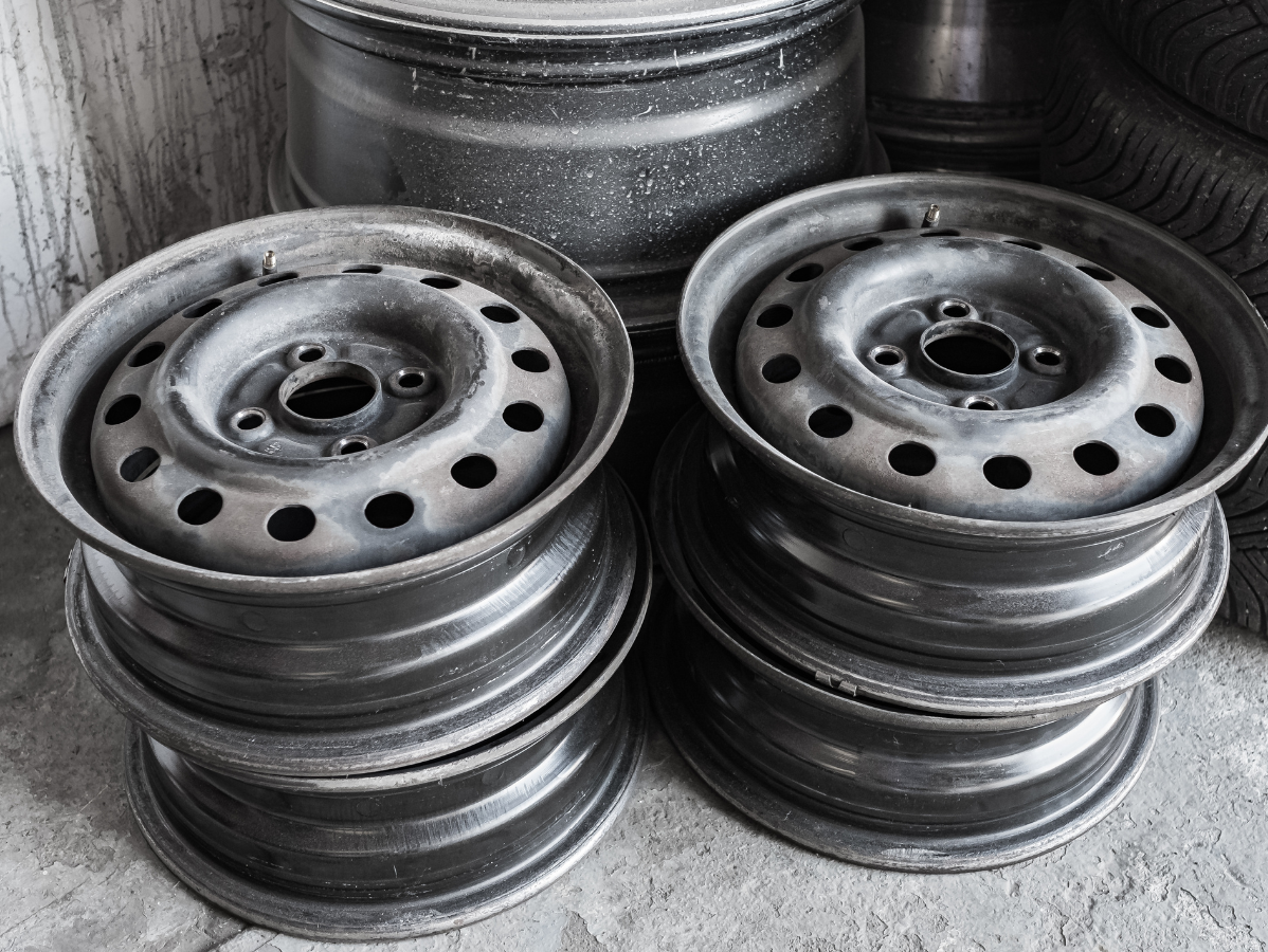 Four stacked steel car rims, gray and slightly dusty, indoors.