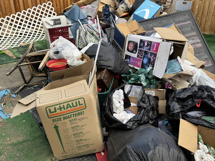 Pile of trash and cardboard boxes in an outdoor setting; U-Haul box visible.