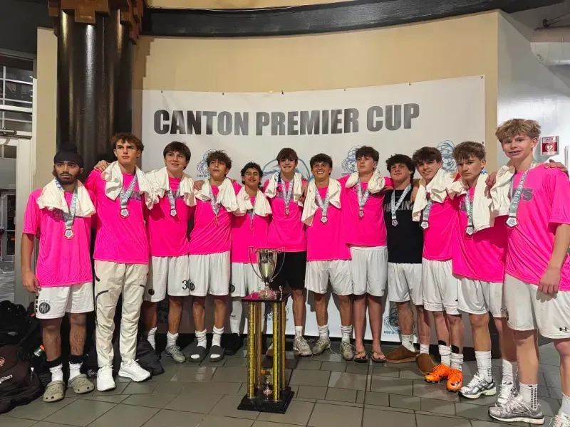 Group of soccer players in pink jerseys posing with a trophy under a “Canton Premier Cup” banner