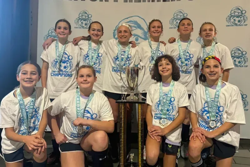Youth dance team posing with a large trophy in front of a branded backdrop