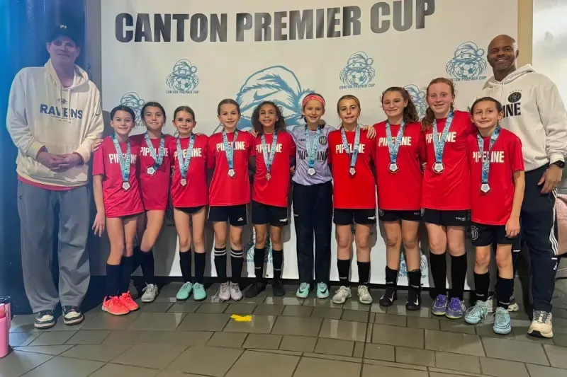 Youth sports team posing with medals in front of a Canton Premier Cup banner