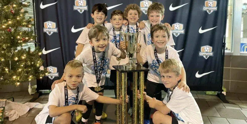 A group of young boys are posing for a picture with a trophy.