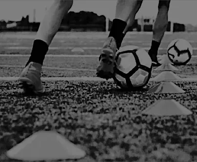 a black and white photo of a person kicking a soccer ball on a field .