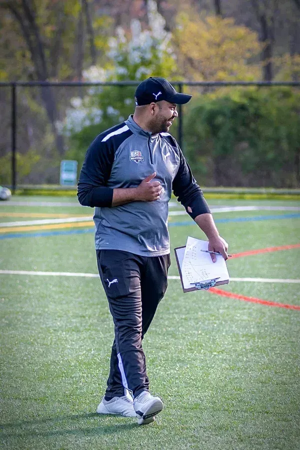 Coppermine Soccer Club's coach walking on the field evaluating youth club soccer players during a tryout session.