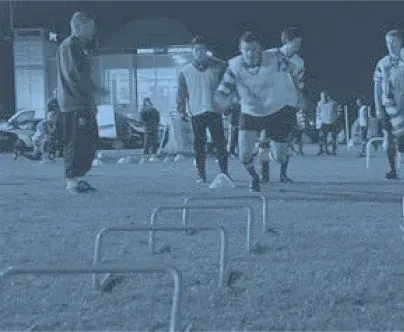 a group of soccer players are running over hurdles on a field .