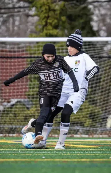 Two soccer players in black and white uniforms compete for the ball on a field.