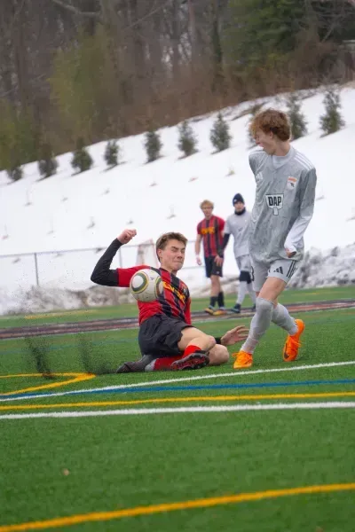 Soccer players contesting a ball on a snowy field, one sliding while another prepares to kick.