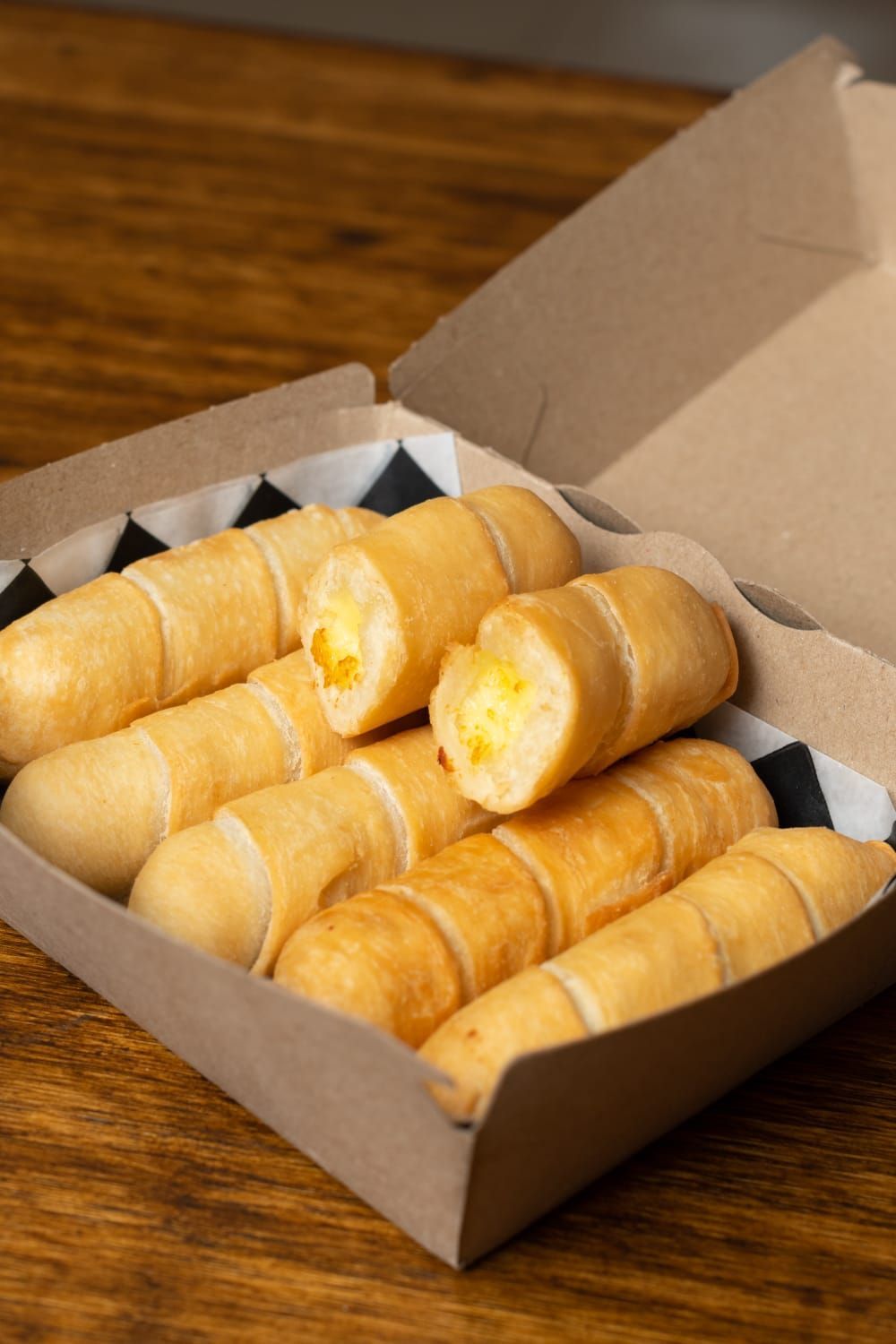 Caja de tequeños fritos dorados sobre una mesa de madera.