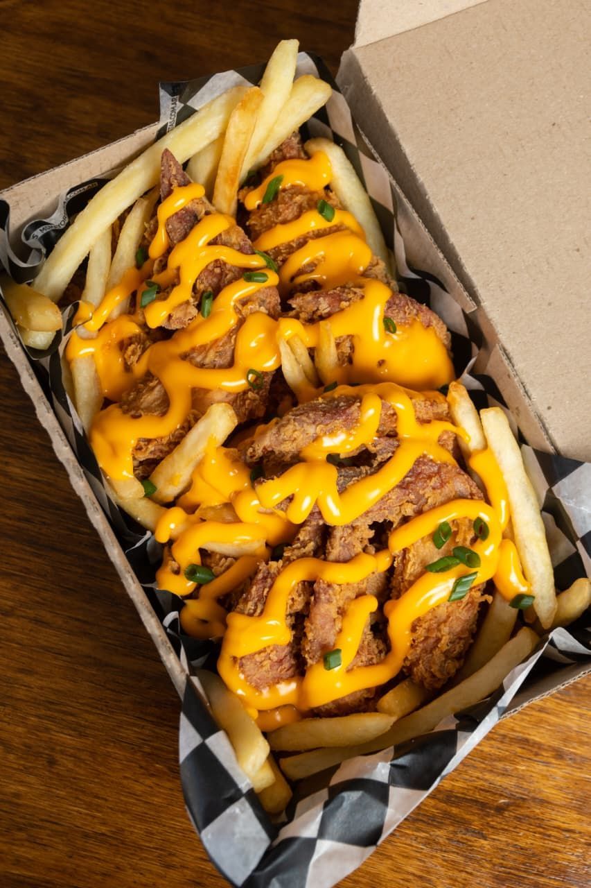 Pollo y papas fritas en caja, rociados con salsa de naranja y guarnición verde.